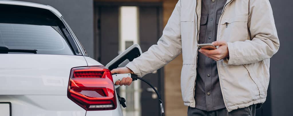 A man looks at his phone whilst charging his electric vehicle.