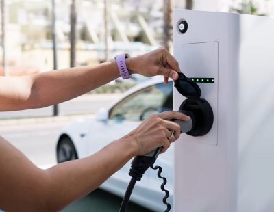 Cropped image of woman connecting electric car cable to power charger in electric vehicle parking